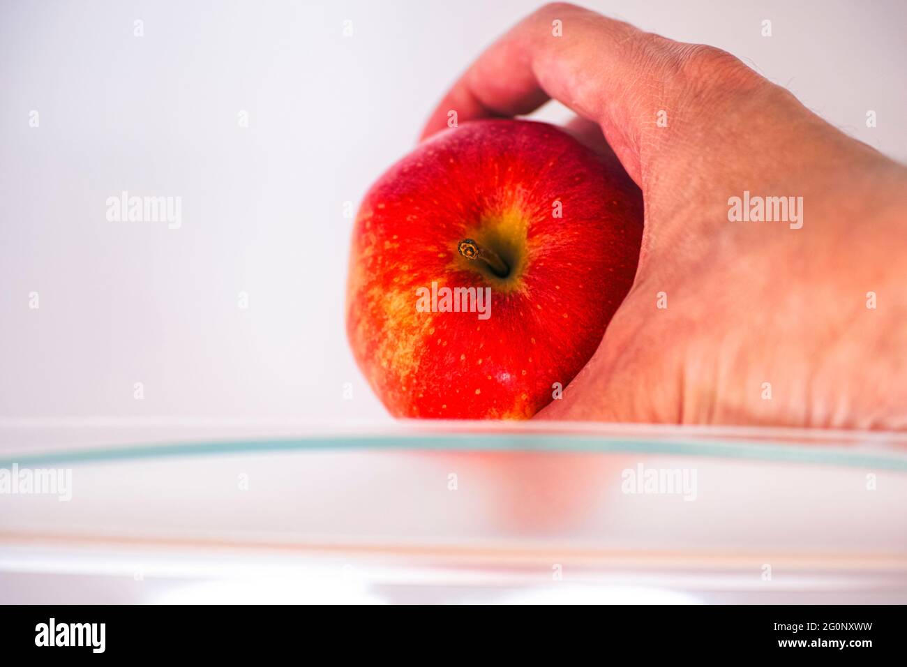 Mano di persona che prende la mela rossa dal ripiano del frigorifero. Primo piano. Foto Stock