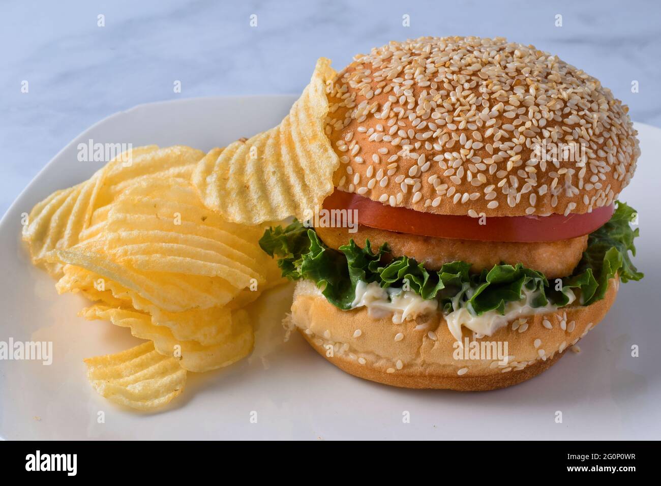 hamburger di salmone su un panino di condimento con un lato di patatine fritte Foto Stock