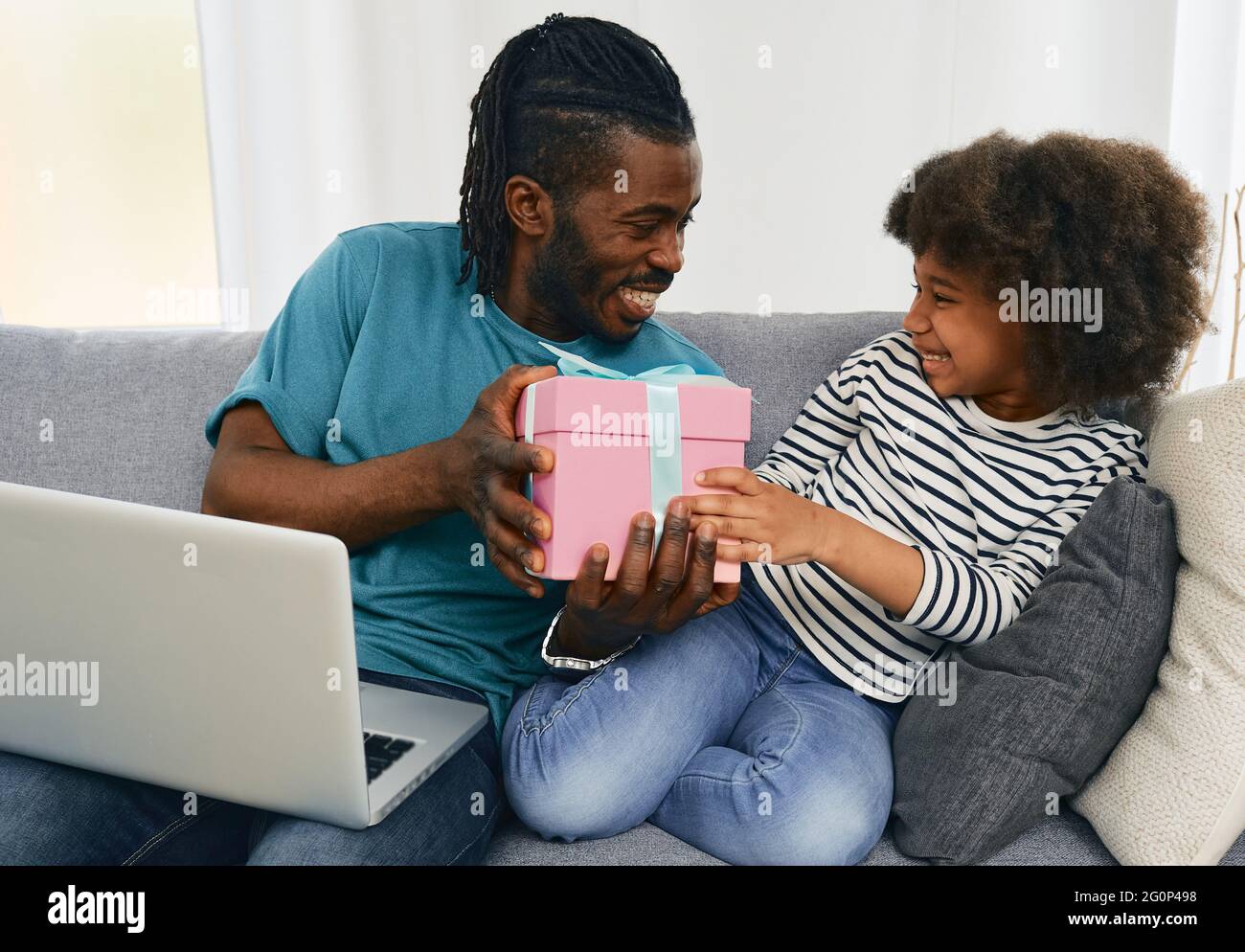 Il padre afroamericano dà alla figlia un regalo di compleanno che ha ordinato su Internet dal suo laptop. Papà positivo comunica con il bambino, Foto Stock