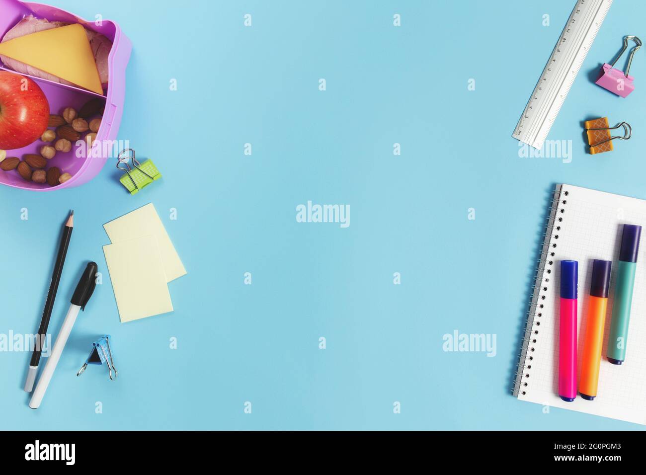 Concetto di piatto della scuola primaria con le forniture assortite della scuola, blocco note, penna, matita, mercati, adesivi, clip di carta e scatola per pranzo con sandwich, dadi Foto Stock