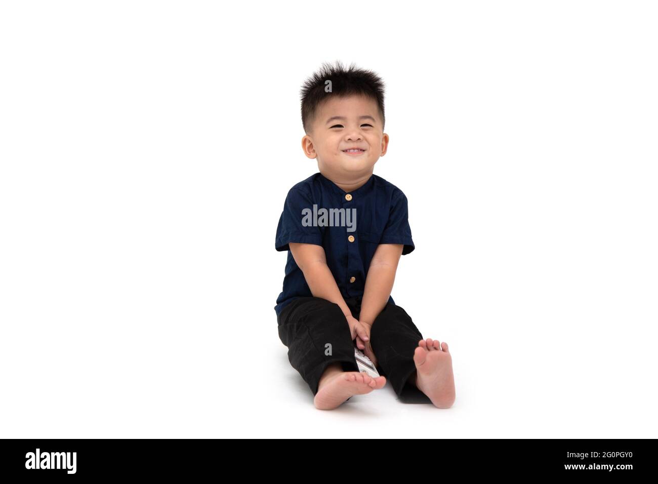 Ritratto di un bambino asiatico seduto sul pavimento che guarda timido e sorridente isolato su uno sfondo bianco, 1 anno 10 mesi Foto Stock