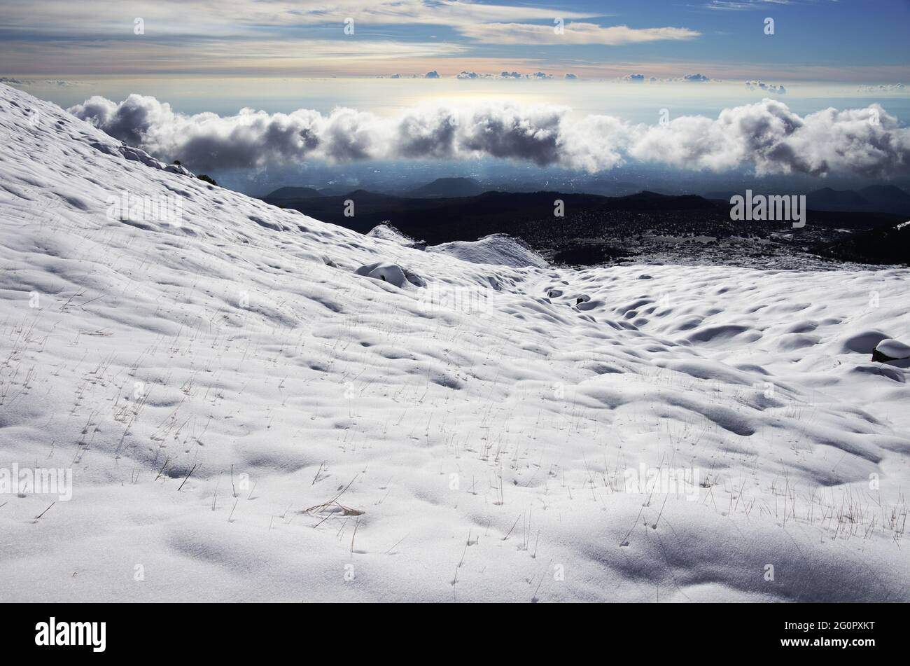 Versante montano dell'Etna coperto di neve in Sicilia bianche e basse nuvole all'orizzonte Foto Stock