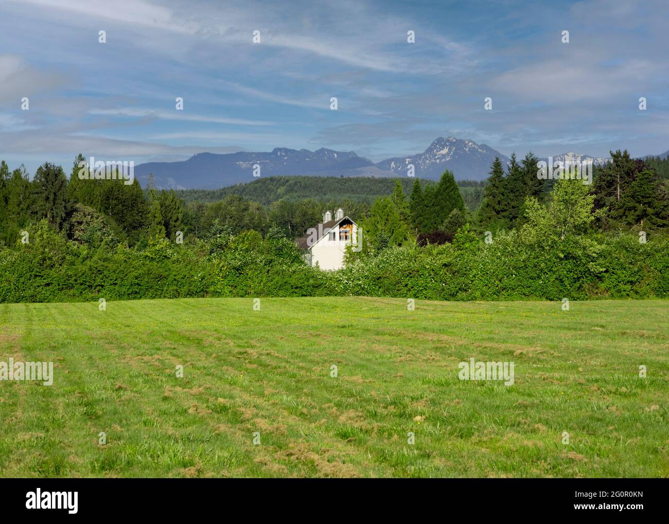 Casa in stile fattoria con le montagne a cascata sullo sfondo. Foto Stock