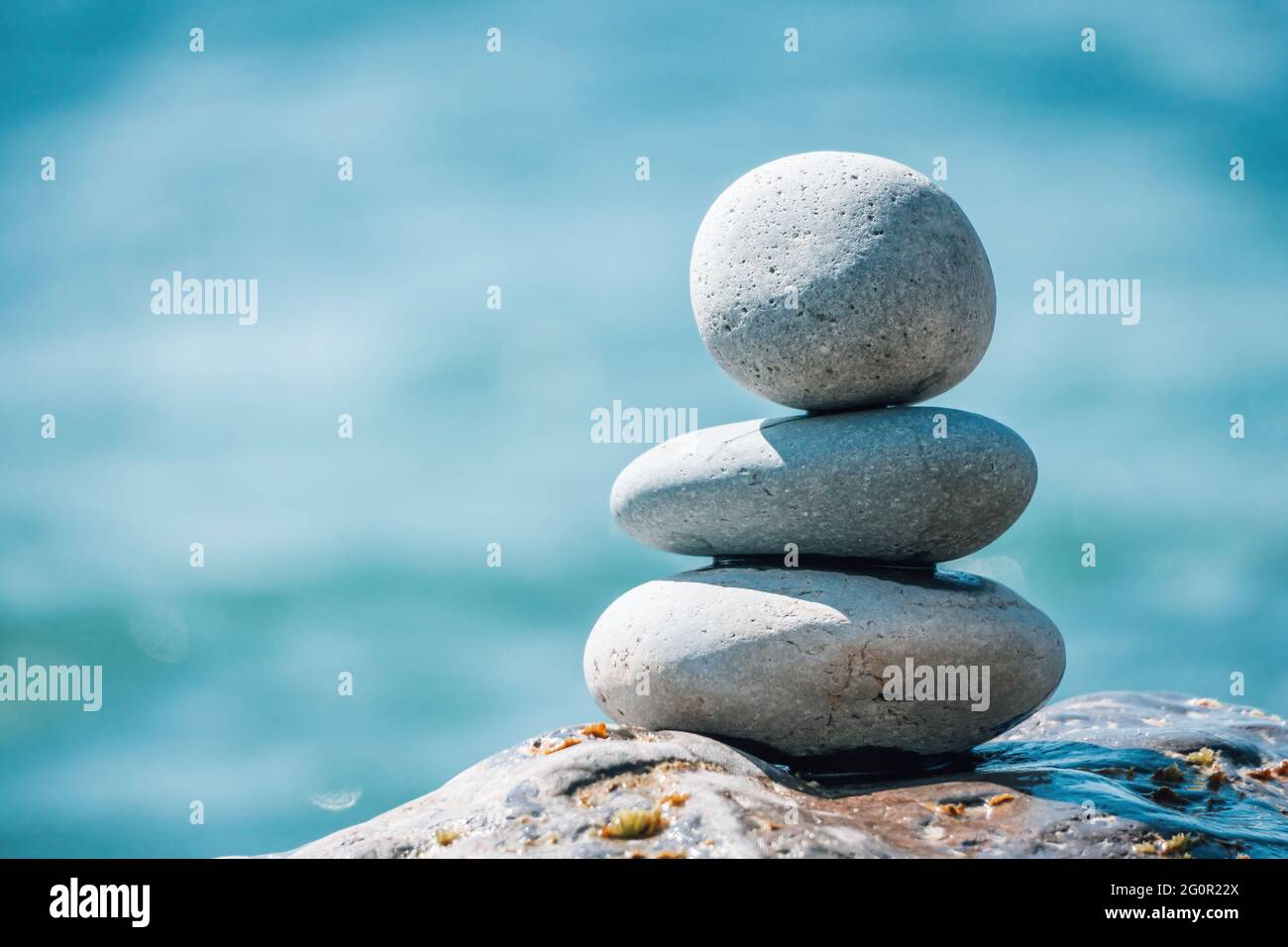 Equilibrata piramide di ciottoli sulla spiaggia in una giornata di sole. Abstract Sea bokeh sullo sfondo. Messa a fuoco selettiva. Pietre Zen sulla spiaggia di mare, meditazione Foto Stock