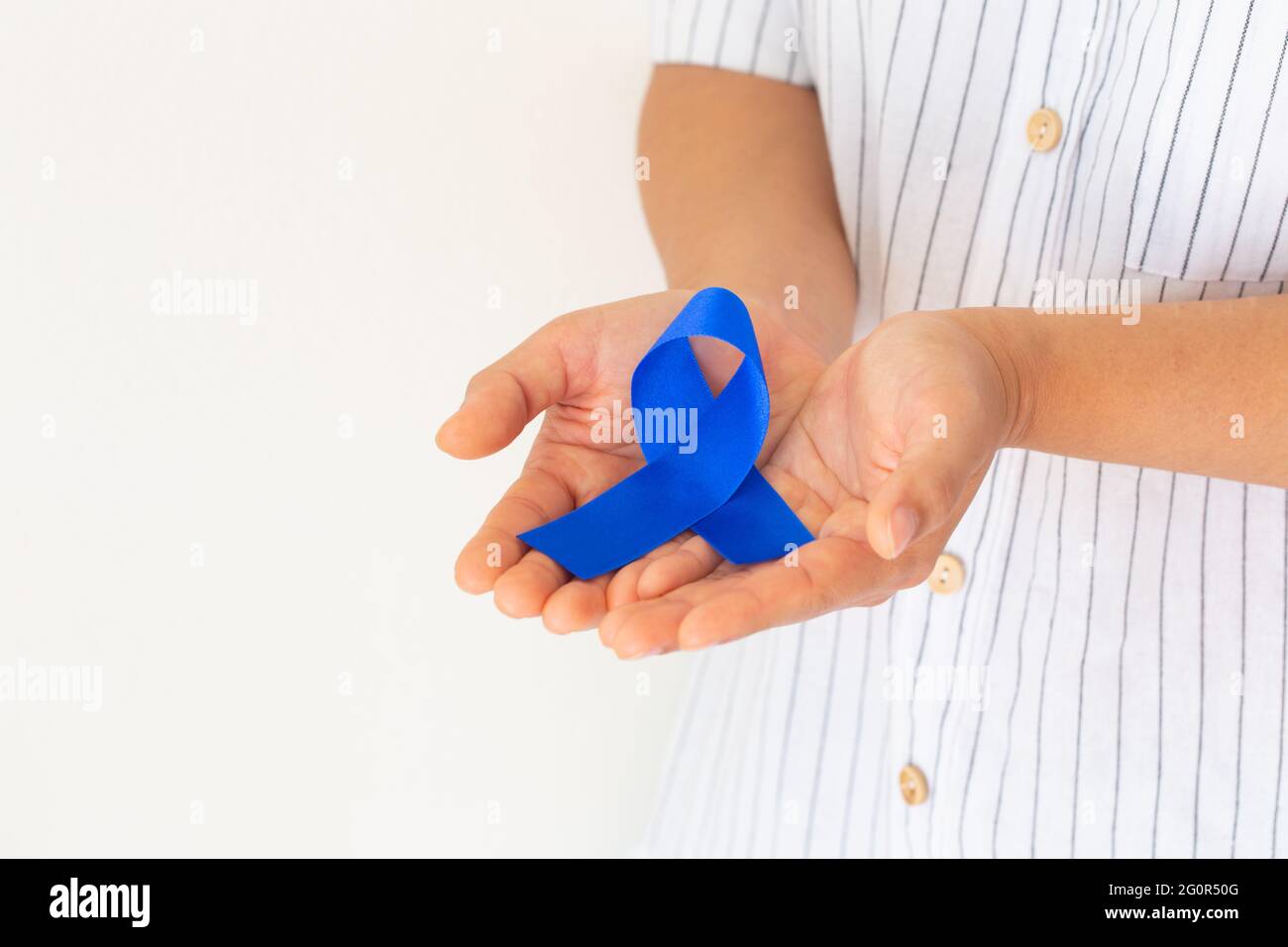 Mani che tengono il nastro blu profondo su tessuto bianco con spazio per la copia. Consapevolezza del cancro colorettale, cancro del colon della persona anziana e giornata mondiale del diabete, Chil Foto Stock