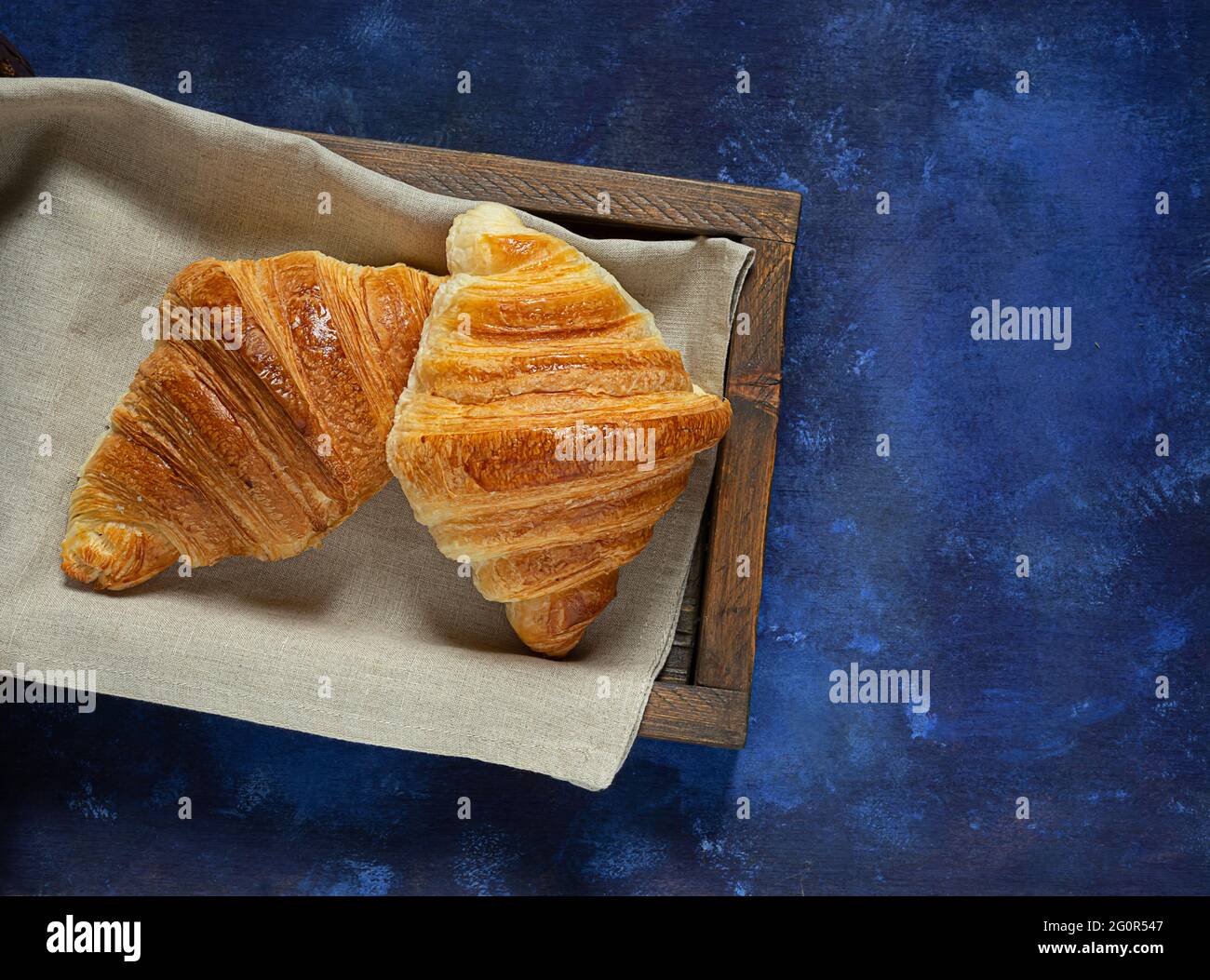 Croissant francesi freschi in vassoio di legno su sfondo blu, vista dall'alto Foto Stock