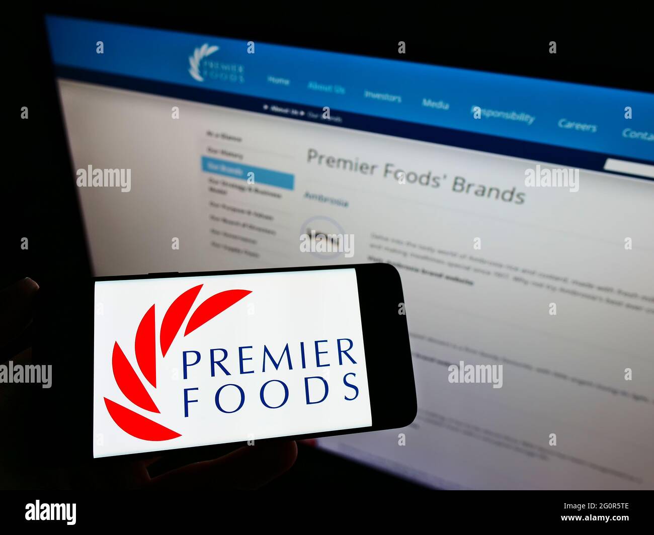 Persona che tiene il telefono cellulare con il logo del produttore britannico di alimenti Premier Foods plc sullo schermo di fronte al sito web della società. Mettere a fuoco il display del telefono. Foto Stock