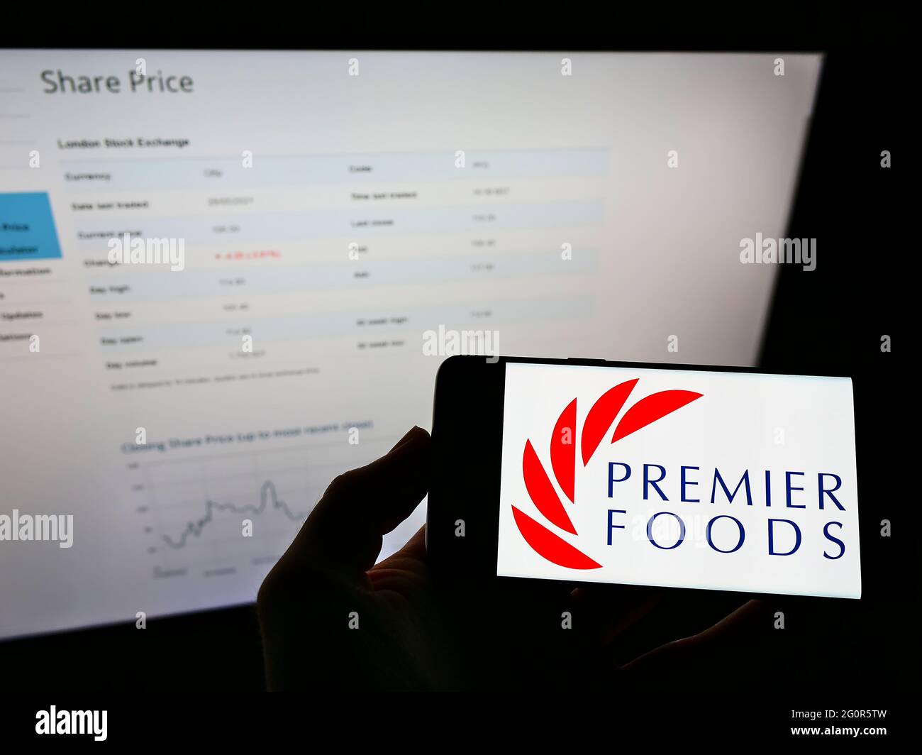 Persona che tiene il cellulare con il logo del produttore britannico di alimenti Premier Foods plc sullo schermo davanti alla pagina web di affari. Mettere a fuoco il display del telefono. Foto Stock