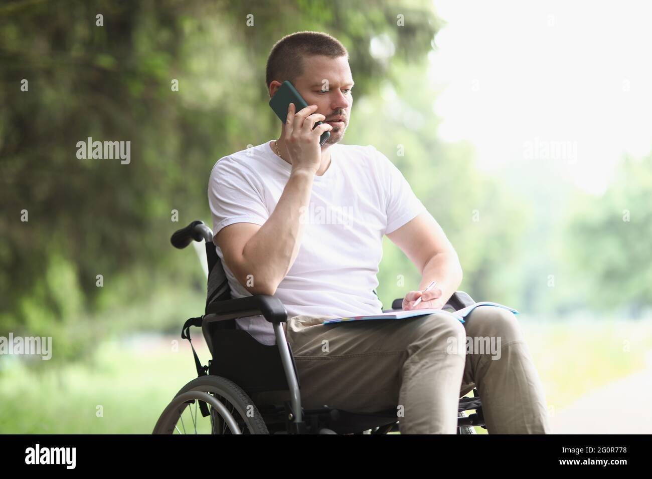 Uomo disabile in sedia a rotelle che parla sul telefono cellulare nel parcheggio Foto Stock