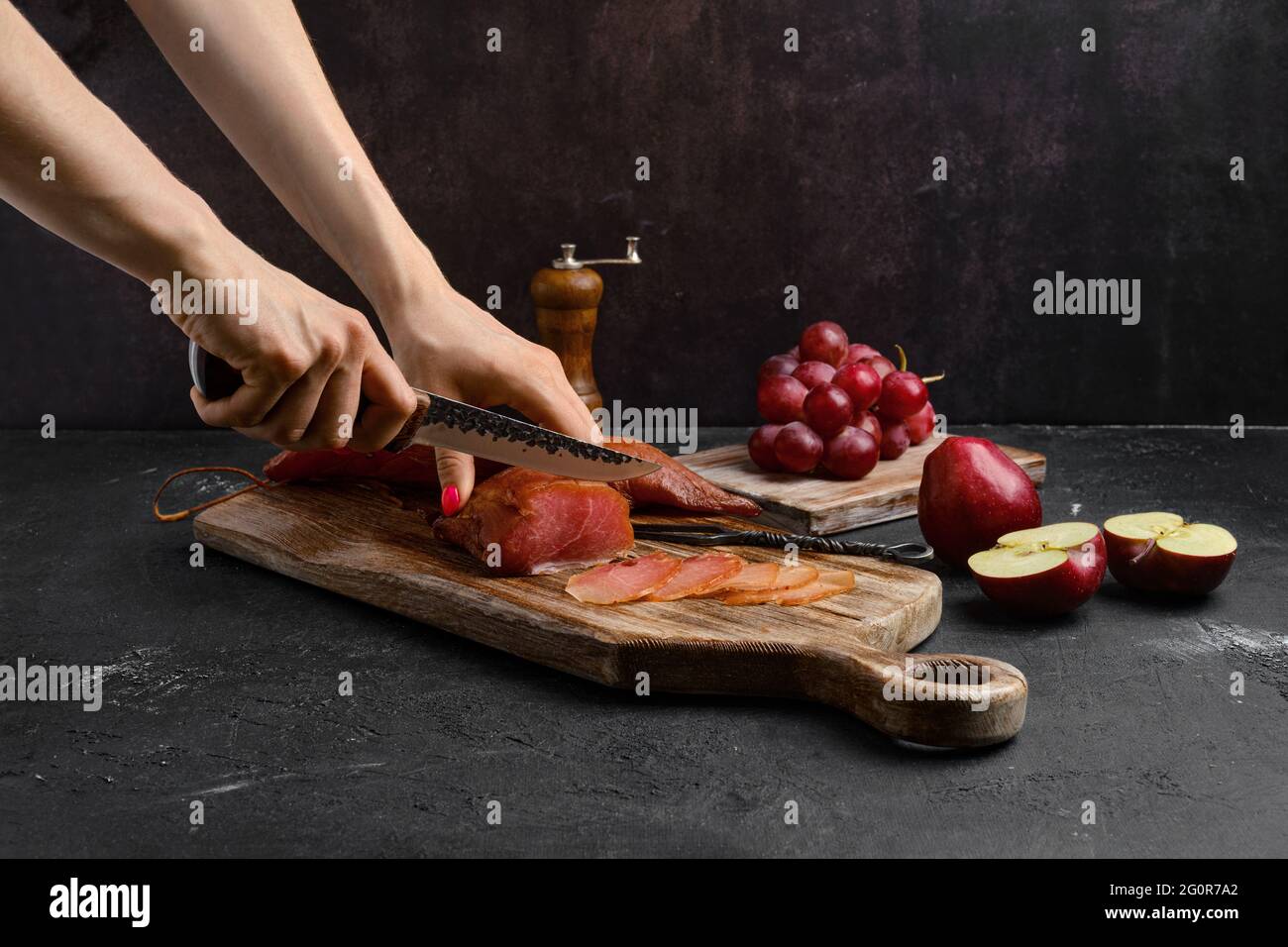 Le mani di una donna tagliano una fetta di aria secca prosciutto di tacchino su tagliere di legno Foto Stock