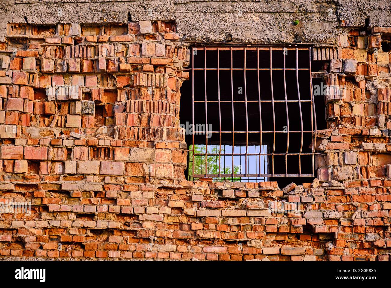 Grata di metallo nel muro di mattoni della casa distrutta; cielo blu attraverso la barriera Foto Stock