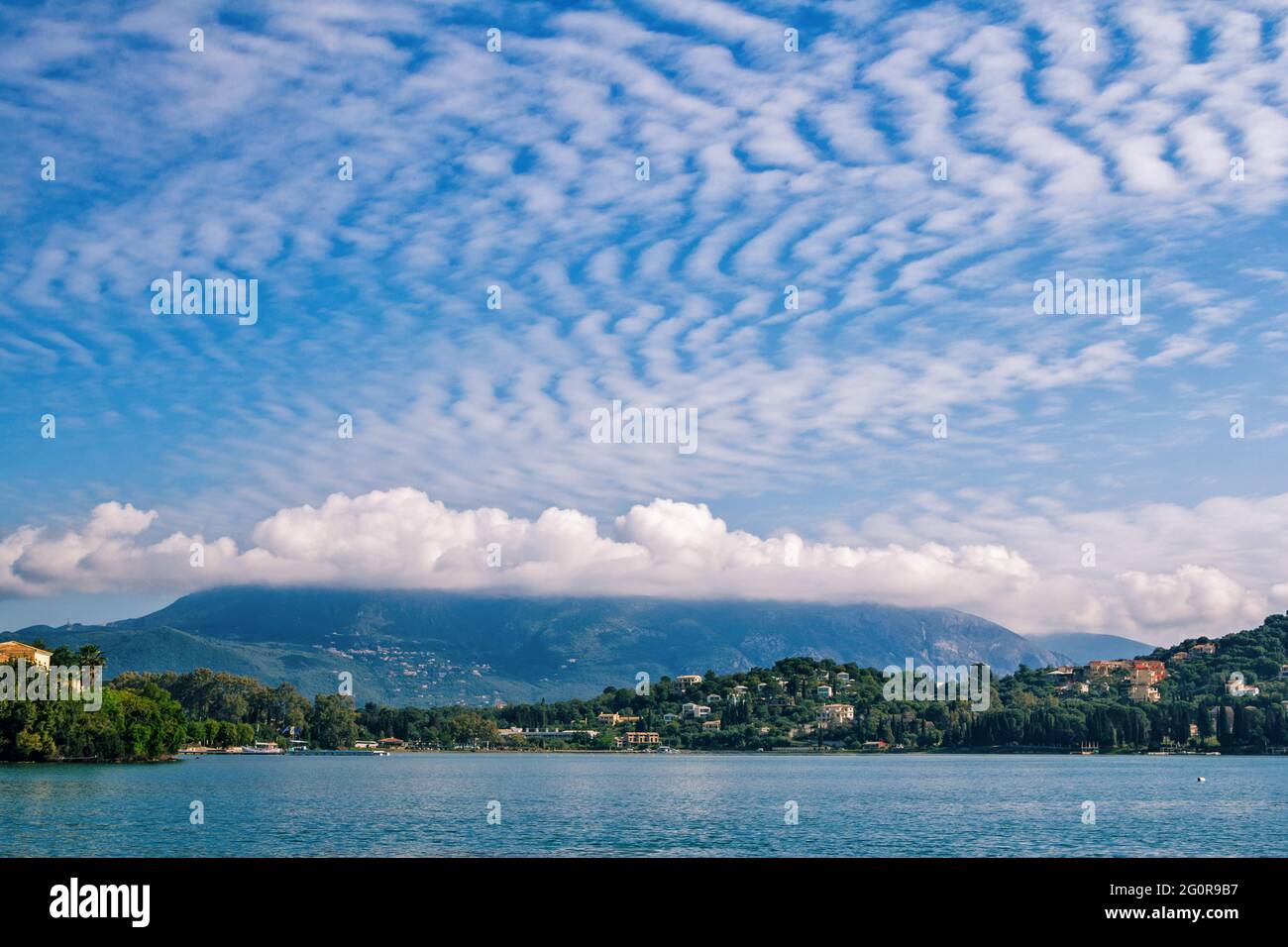 Splendido paesaggio con baia di mare, cielo blu e nuvole bianche, montagne all'orizzonte. Isola di Corfù, Grecia. Foto Stock