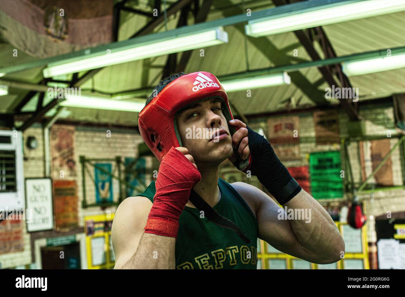 Giovane uomo che mette sulle guardie della testa di boxing che si preparano per la pratica di boxing nel randello di boxing Foto Stock