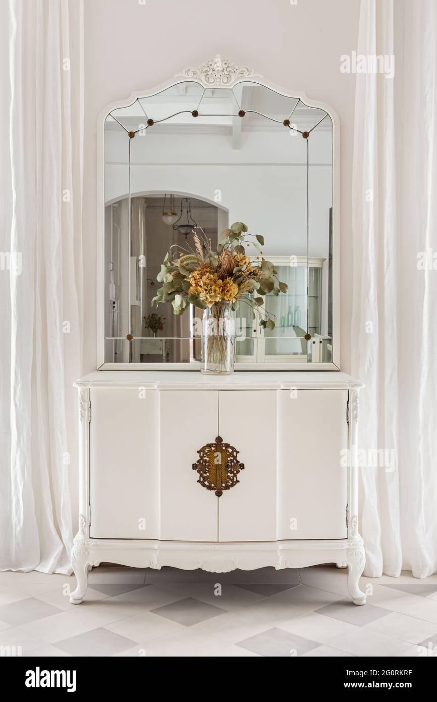 Specchio vintage e bouquet di fiori su armadio in legno. Mobili antichi  restaurati in interni classici e luminosi con pareti e tende bianche Foto  stock - Alamy
