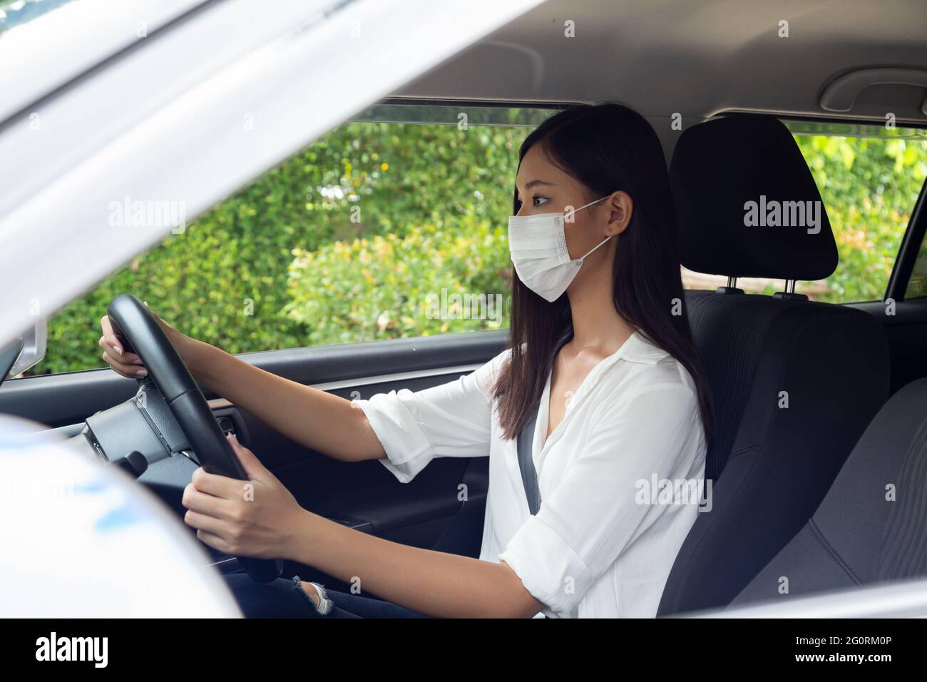 Giovane donna asiatica che guida e indossa la maschera e si siede in auto Foto Stock