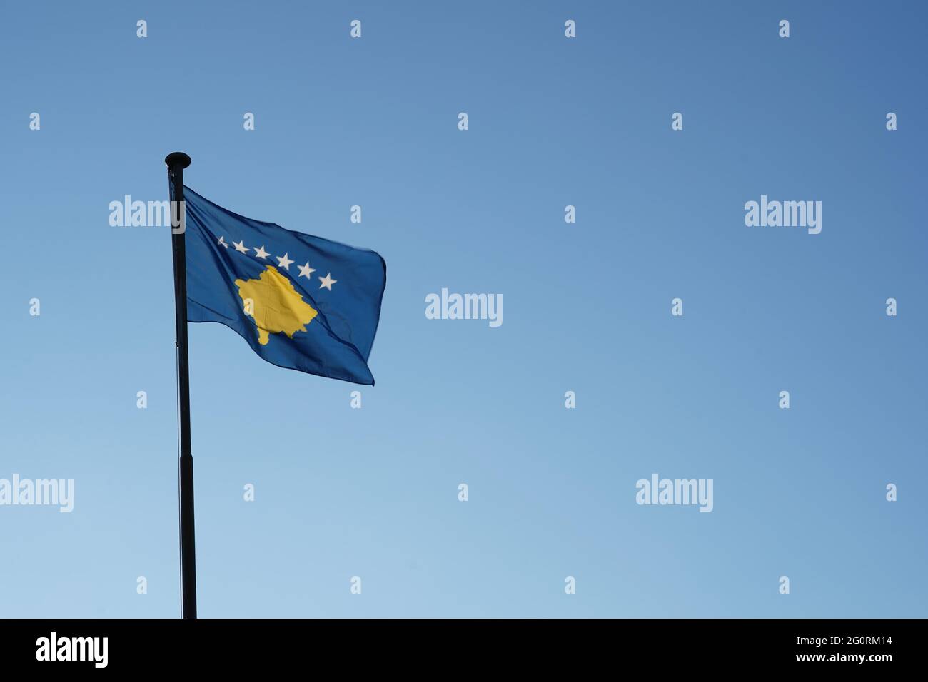 Bandiera del Kosovo issata su un flagpole che ondeggiava nel vento. Vista ad angolo basso rispetto al cielo blu con ampio spazio per la copia. Foto Stock