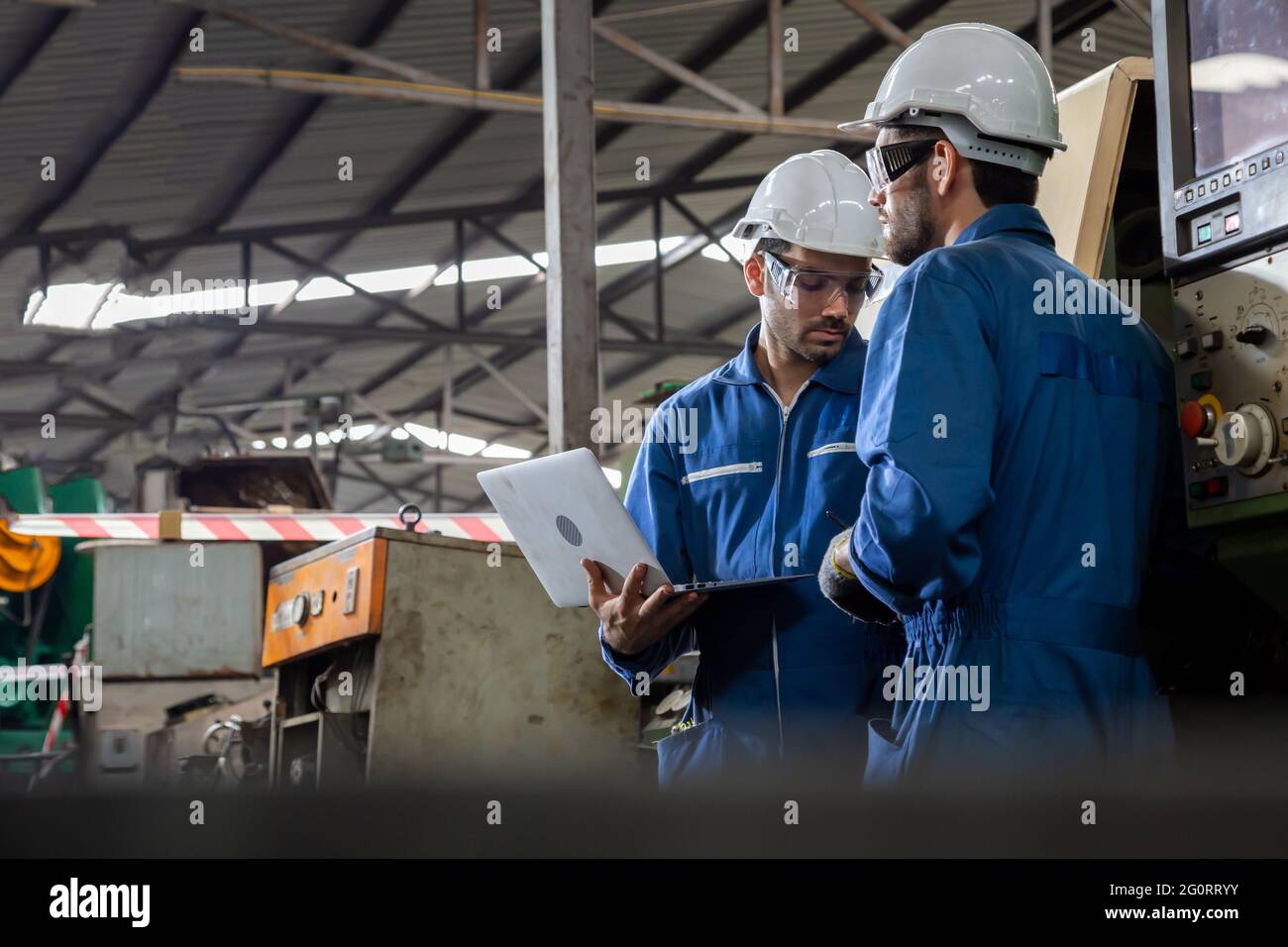 Tecnico di fabbrica che controlla la macchina e legge il rapporto da computer portatile, concetto di manutenzione annuale Foto Stock