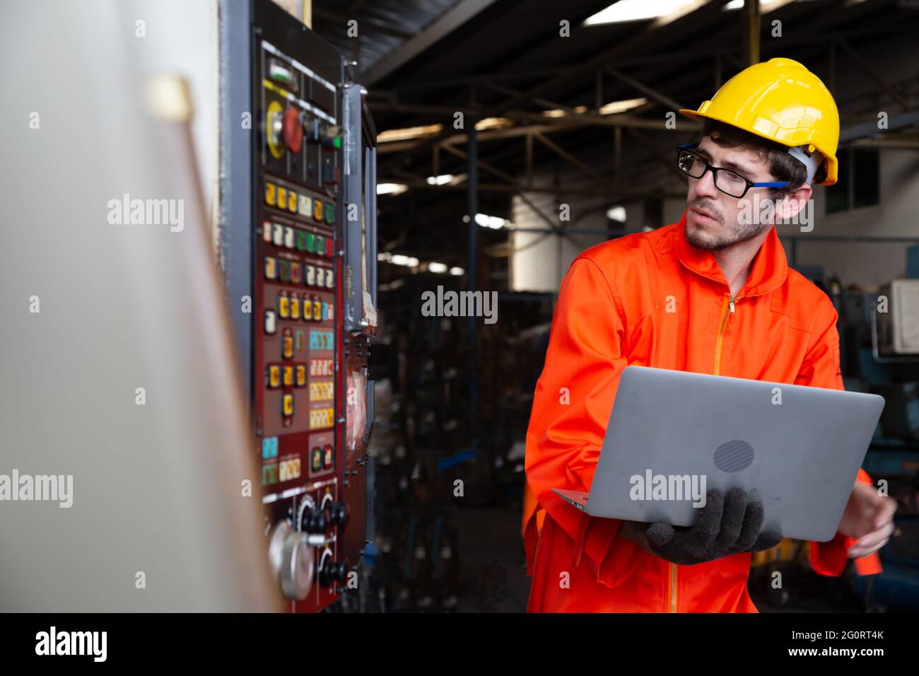 Capo ingegnere che indossa un elmetto in fabbrica e che tiene un laptop, bel lavoratore uomo in un ambiente industriale pesante Foto Stock