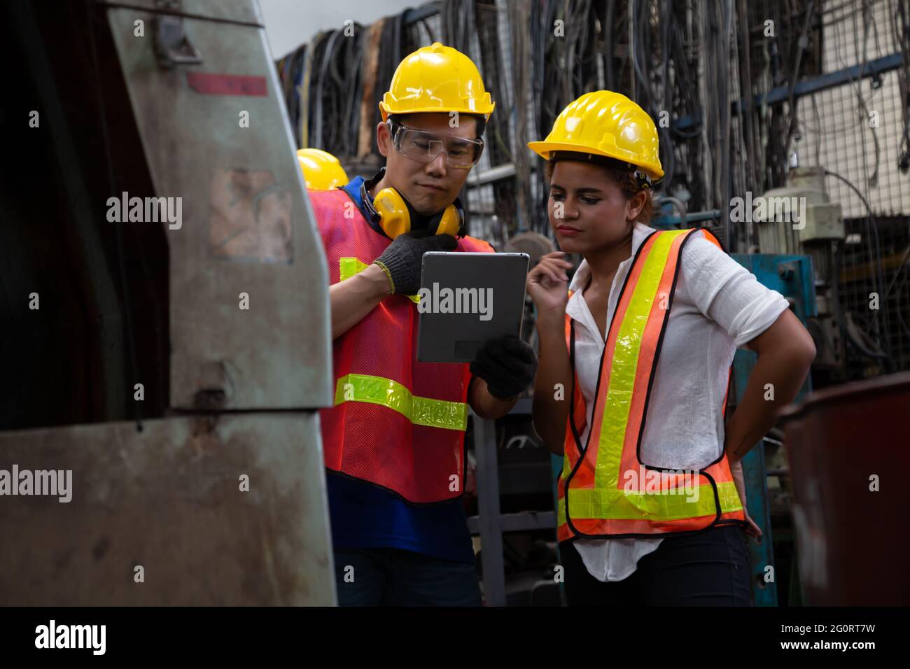 Ingegnere di fabbrica che indossa un elmetto giallo e verifica della macchina e report di lettura da tablet, concetto di manutenzione annuale Foto Stock