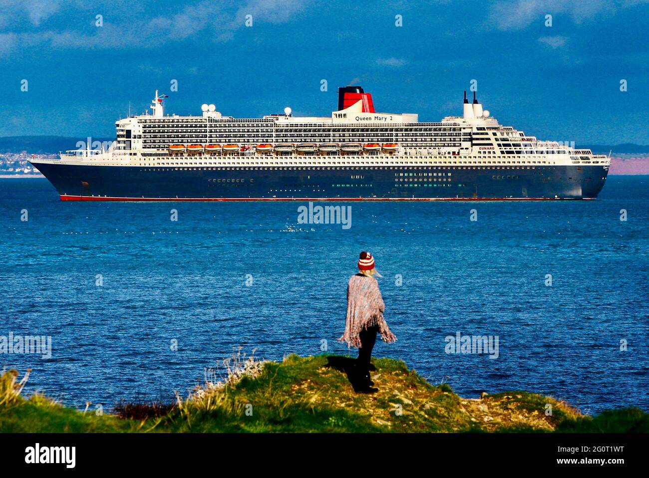 Una donna gode di una vista della magnifica nave da crociera Queen Mary 2 con nave da crociera ancorata al largo di Torbay in Devon, Regno Unito. Foto Stock