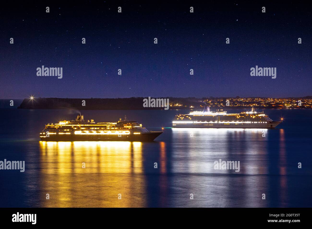 Le navi da crociera Volendam (a sinistra) e P&o Arcadia creano riflessi colorati nel mare al crepuscolo mentre sono ancorate a Torbay in Devon, Regno Unito. Foto Stock