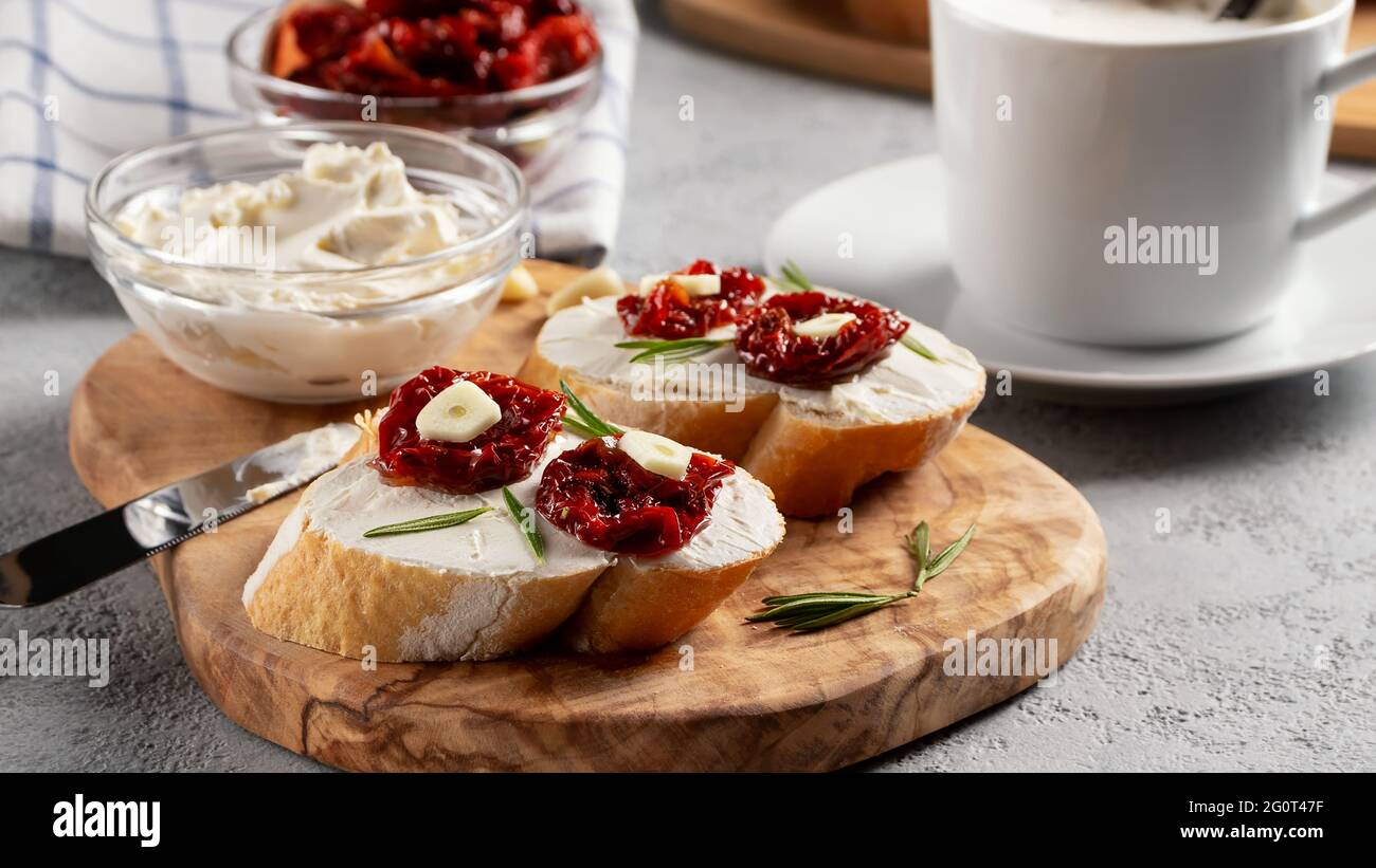 Panini fatti in casa con formaggio spalmabile e pomodori secchi su una tavola di legno di olive - deliziosa colazione salutare, cucina italiana. Foto Stock