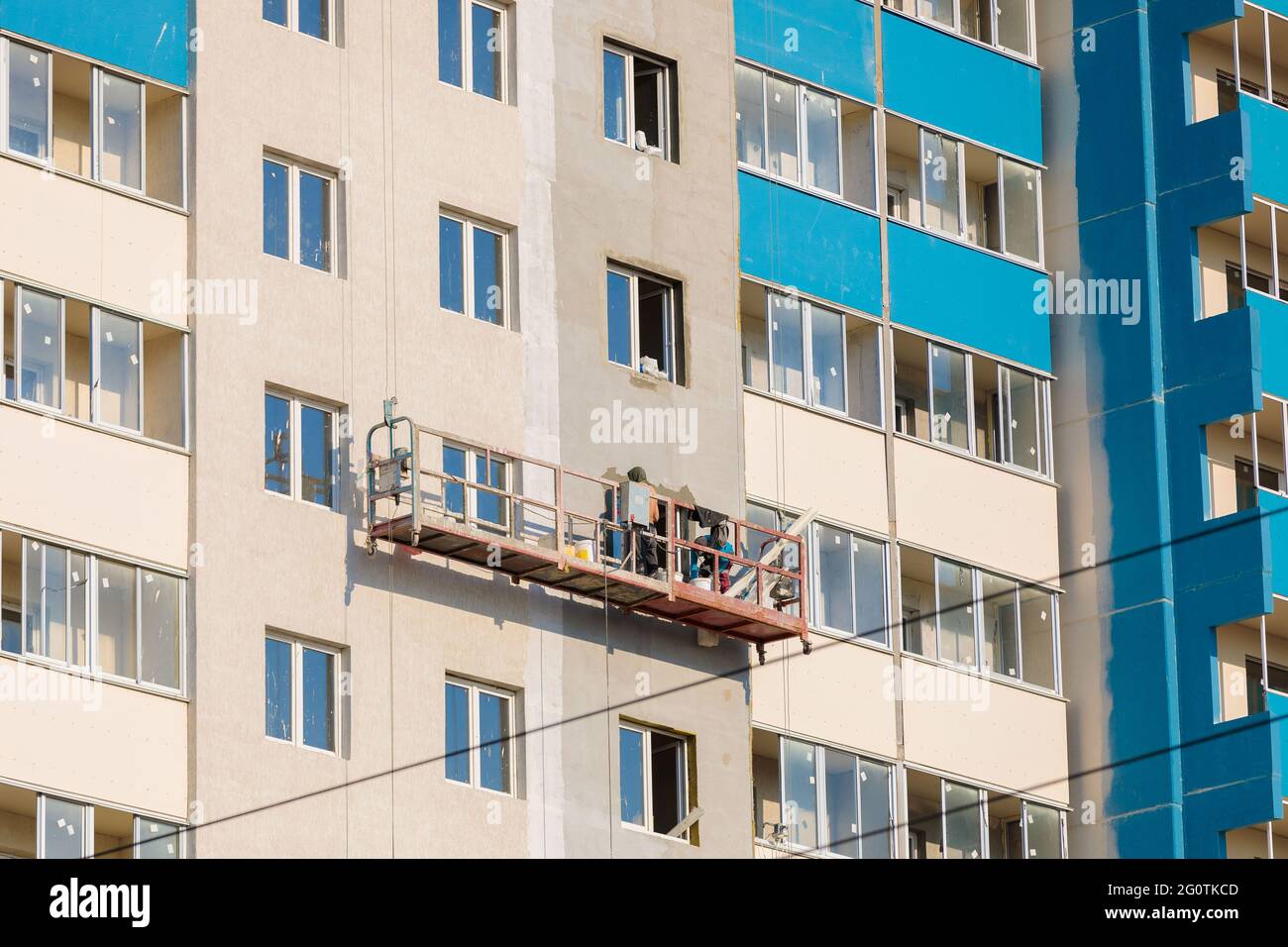 I lavoratori su una piattaforma mobile stanno intonacando le finestre della casa con un mortaio speciale. Foto Stock