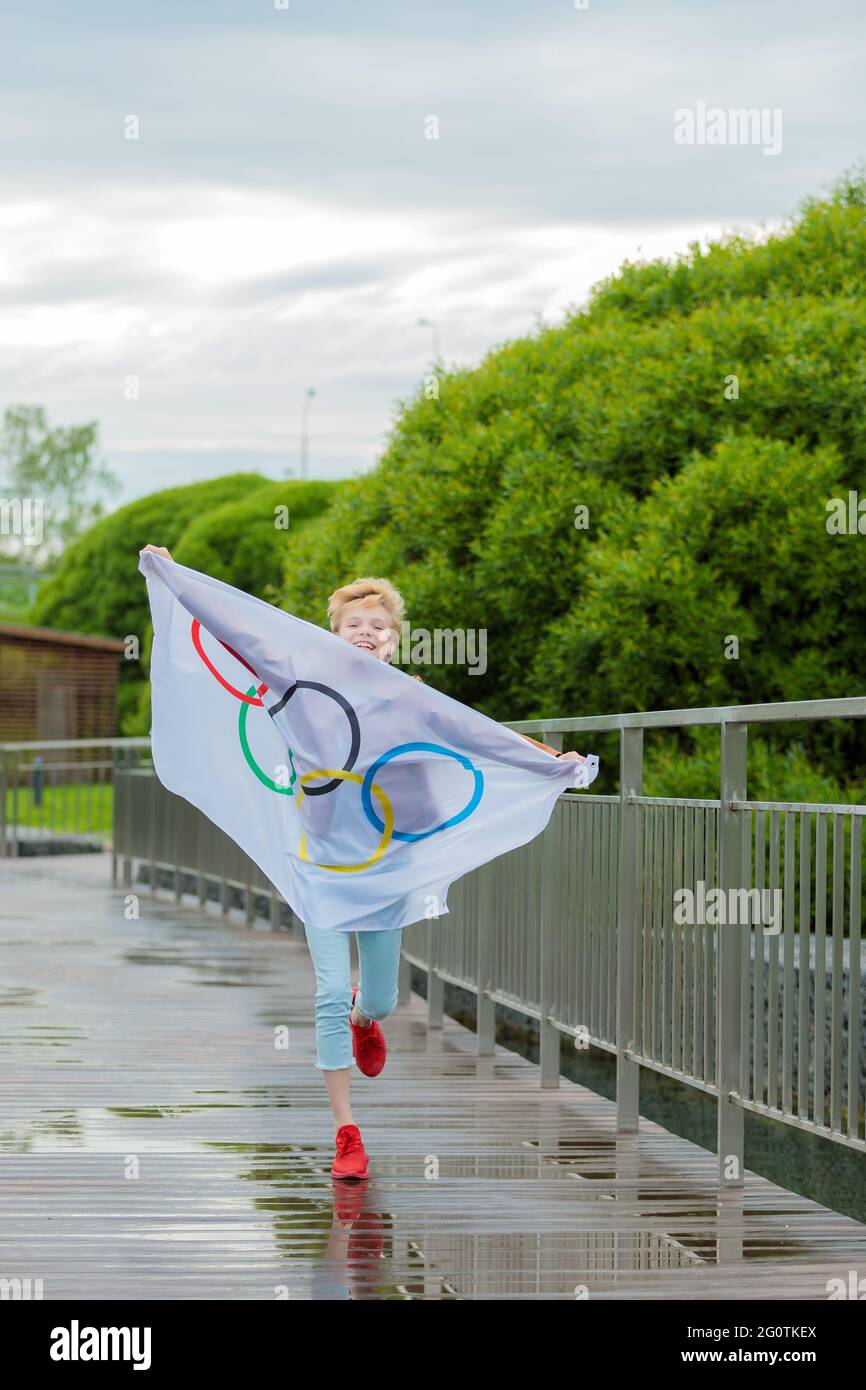 La bionda che sventolava la bandiera olimpica all'aperto nel parco. Giochi Olimpici estivi. Mosca Russia 28 maggio 2021 Foto Stock