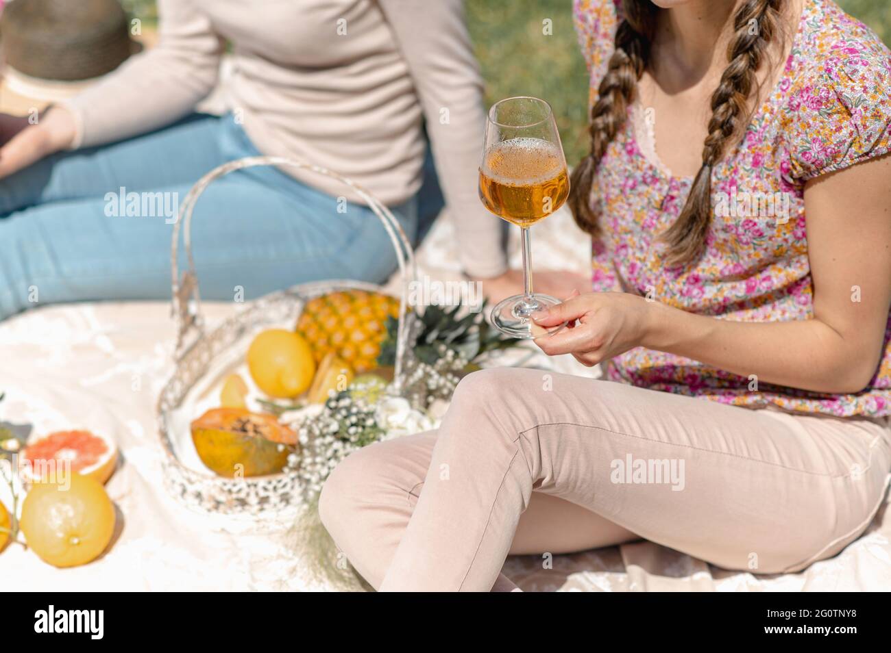 Closeup donna irriconoscibile che tiene un wineglass pieno di vino bianco. Vetro con gocce. Femmine che siedono su una coperta che ha picnic con varietà di f Foto Stock