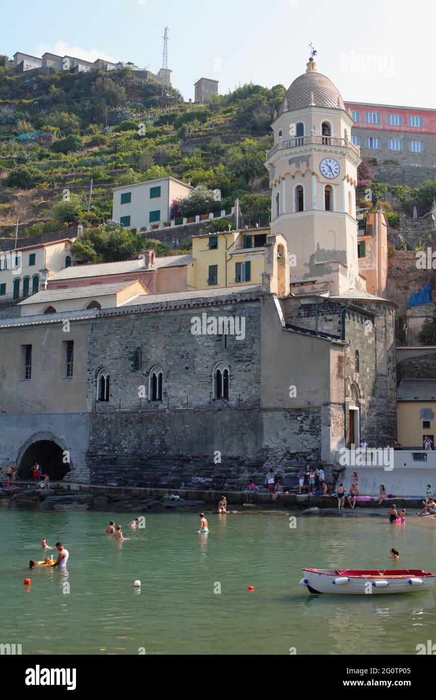 Persone che riposano in mare contro la Chiesa di Santa Margherita d'Antiochia a Vernazza, la Spezia, Liguria, Italia, Parco Nazionale delle cinque Terre Foto Stock
