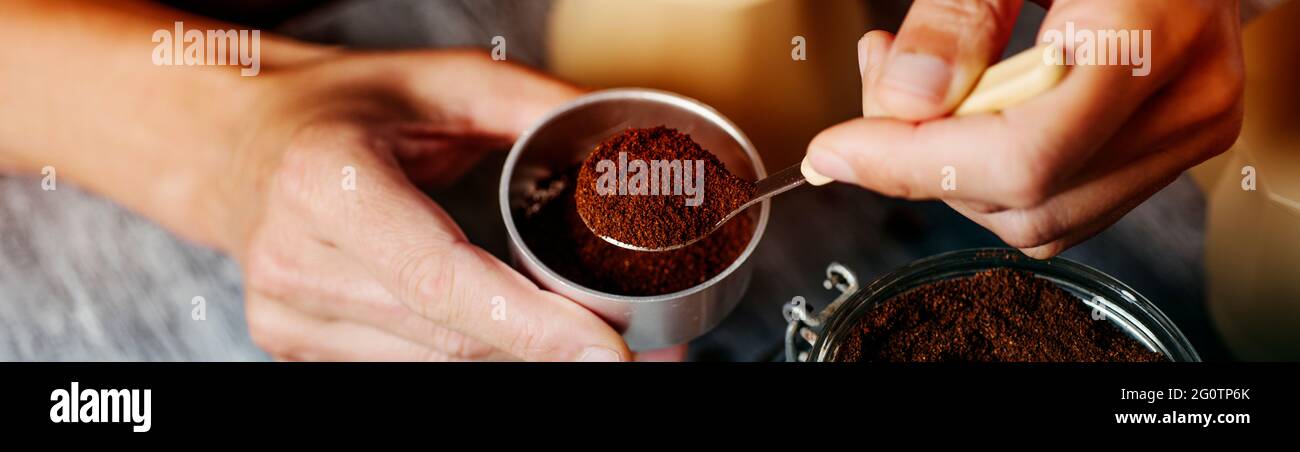 un giovane caucasico riempie l'imbuto di una pentola di moka con caffè macinato, su un tavolo di legno rustico grigio, in un formato panoramico da utilizzare come banner web o. Foto Stock