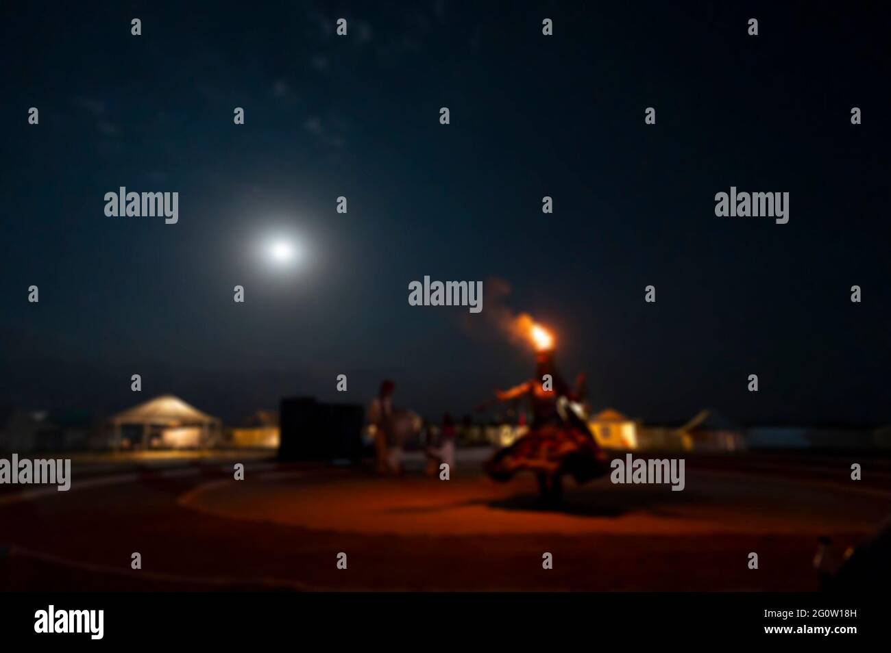 Immagine sfocata della ballerina femminile con ciotola di fuoco sulla testa, vestita con abito culturale del Rajasthan, sotto luna piena di notte al deserto di Thar. Foto Stock