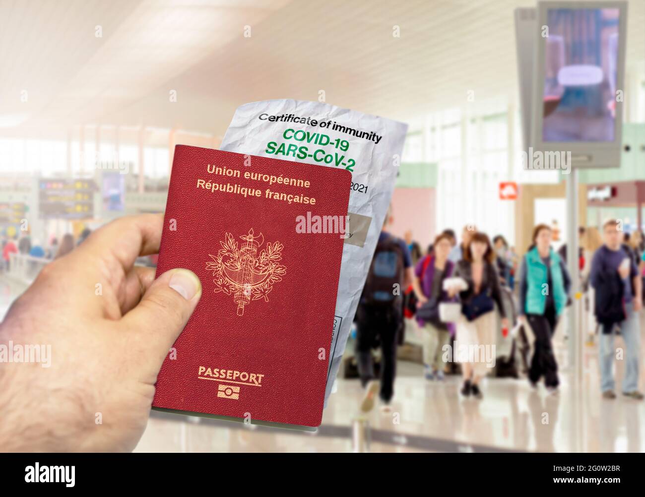 Mano che tiene un passaporto francese con un certificato di immunità Coronavirus Covid 19 di carta stropicciata. Aeroporto offuscato sullo sfondo. Immunità da Covid Foto Stock