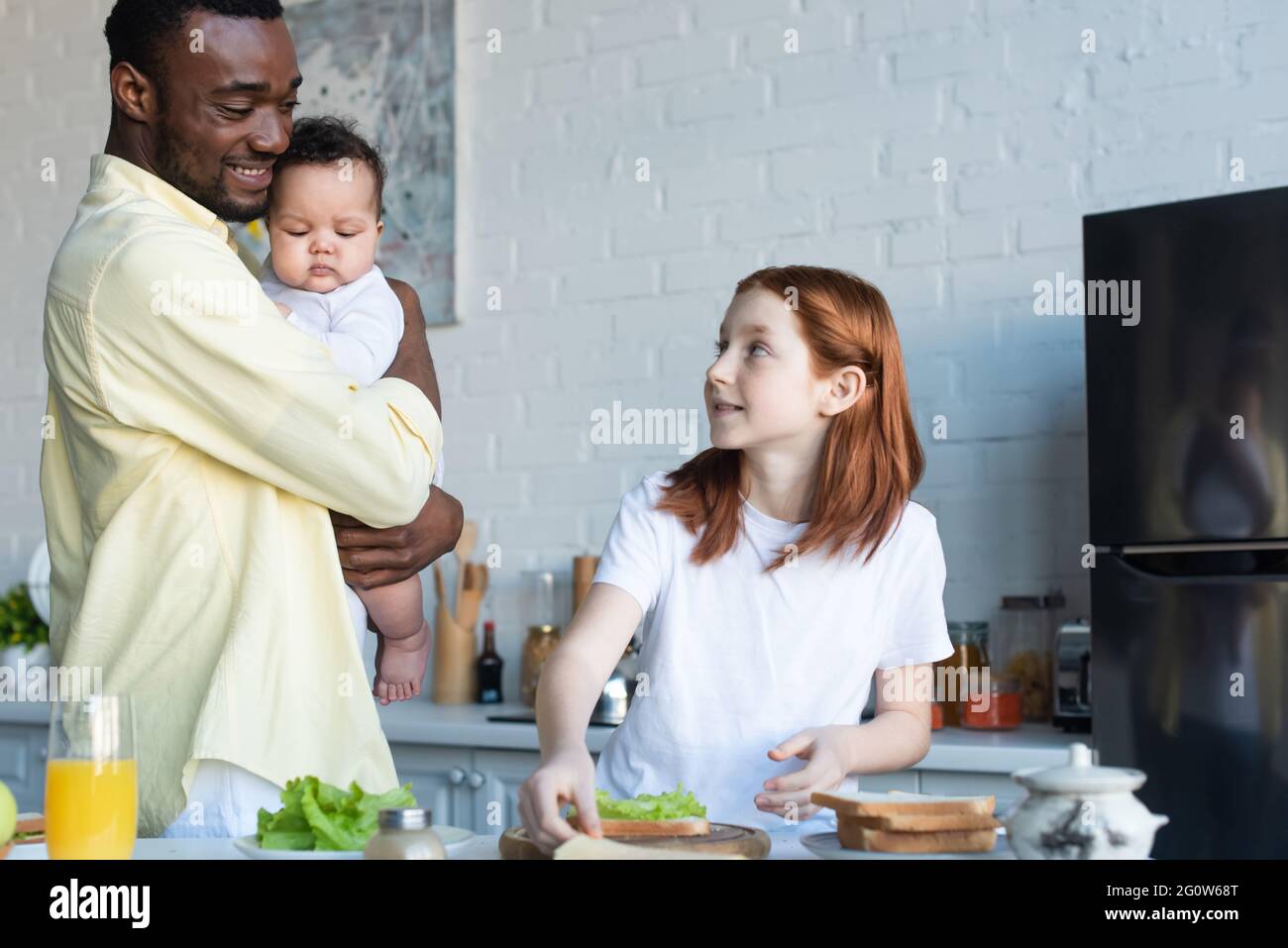 presteen bambino guardando il padre afroamericano con la sorella infantile mentre prepara i panini Foto Stock