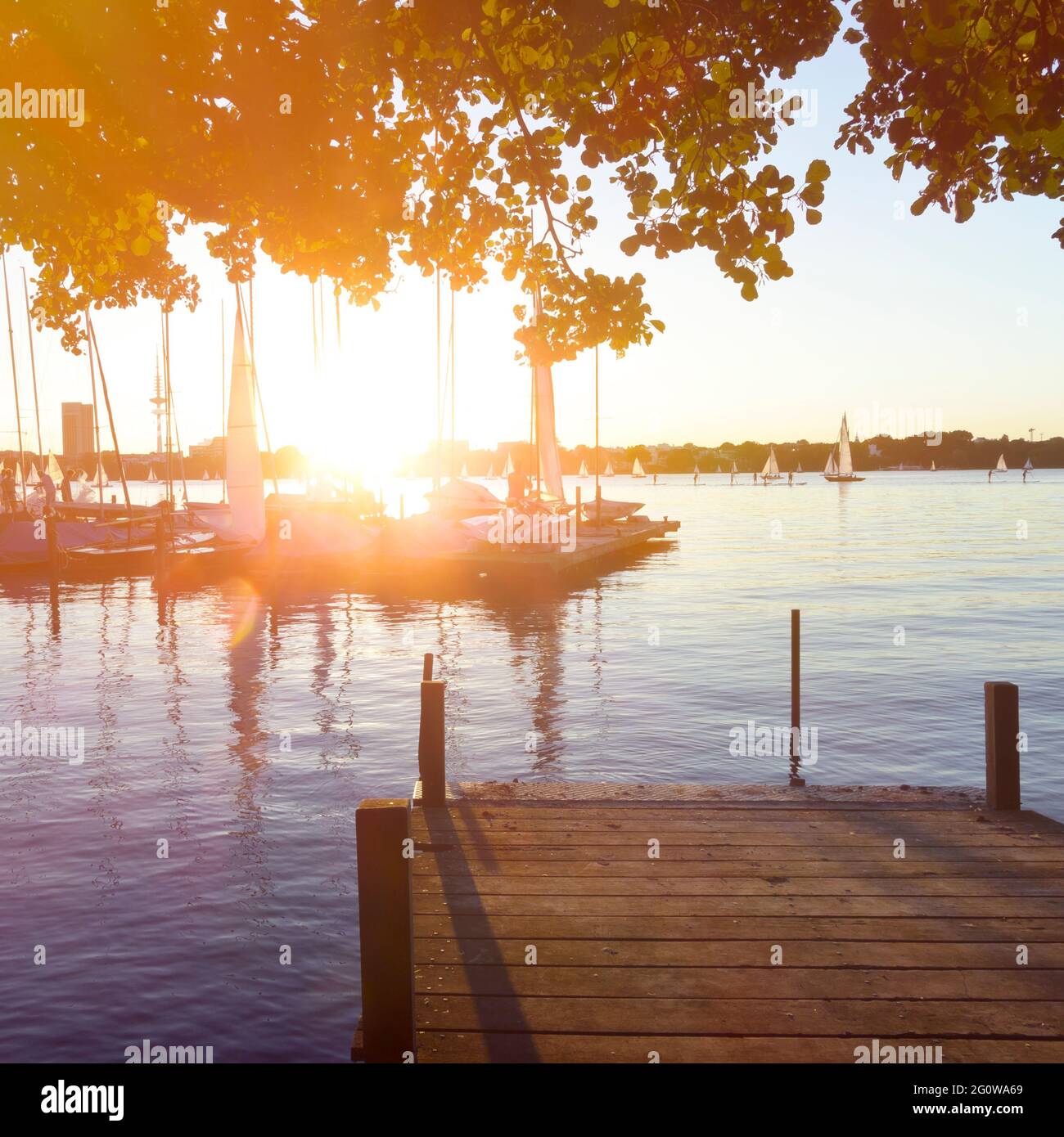 Lago esterno dell'Alster Aussenalster ad Amburgo, Germania, con molo in legno e barche a vela durante un tramonto estivo. Foto Stock