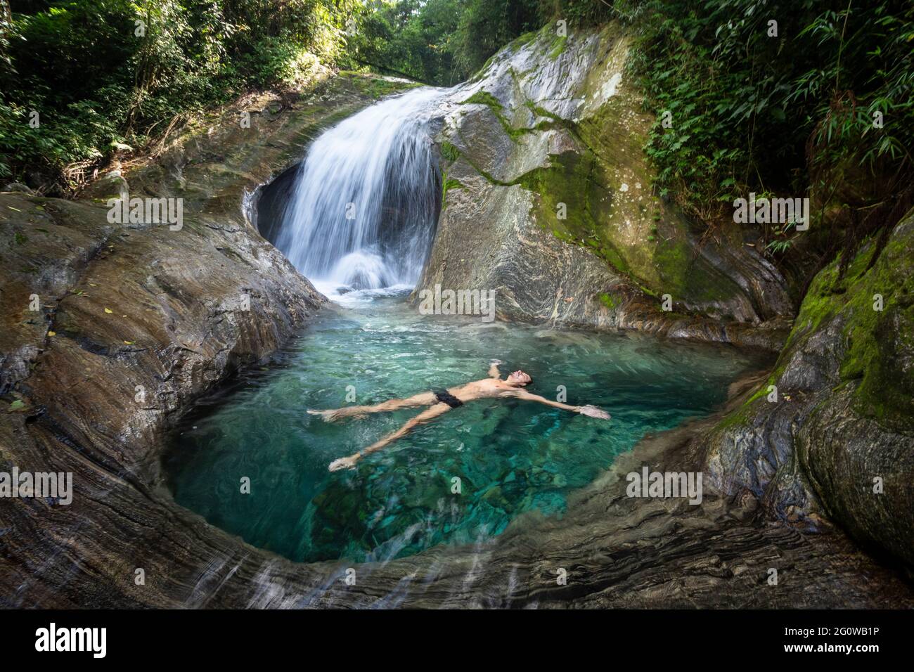 Uomo godendo bella cascata di acqua cristallina della foresta pluviale Foto Stock