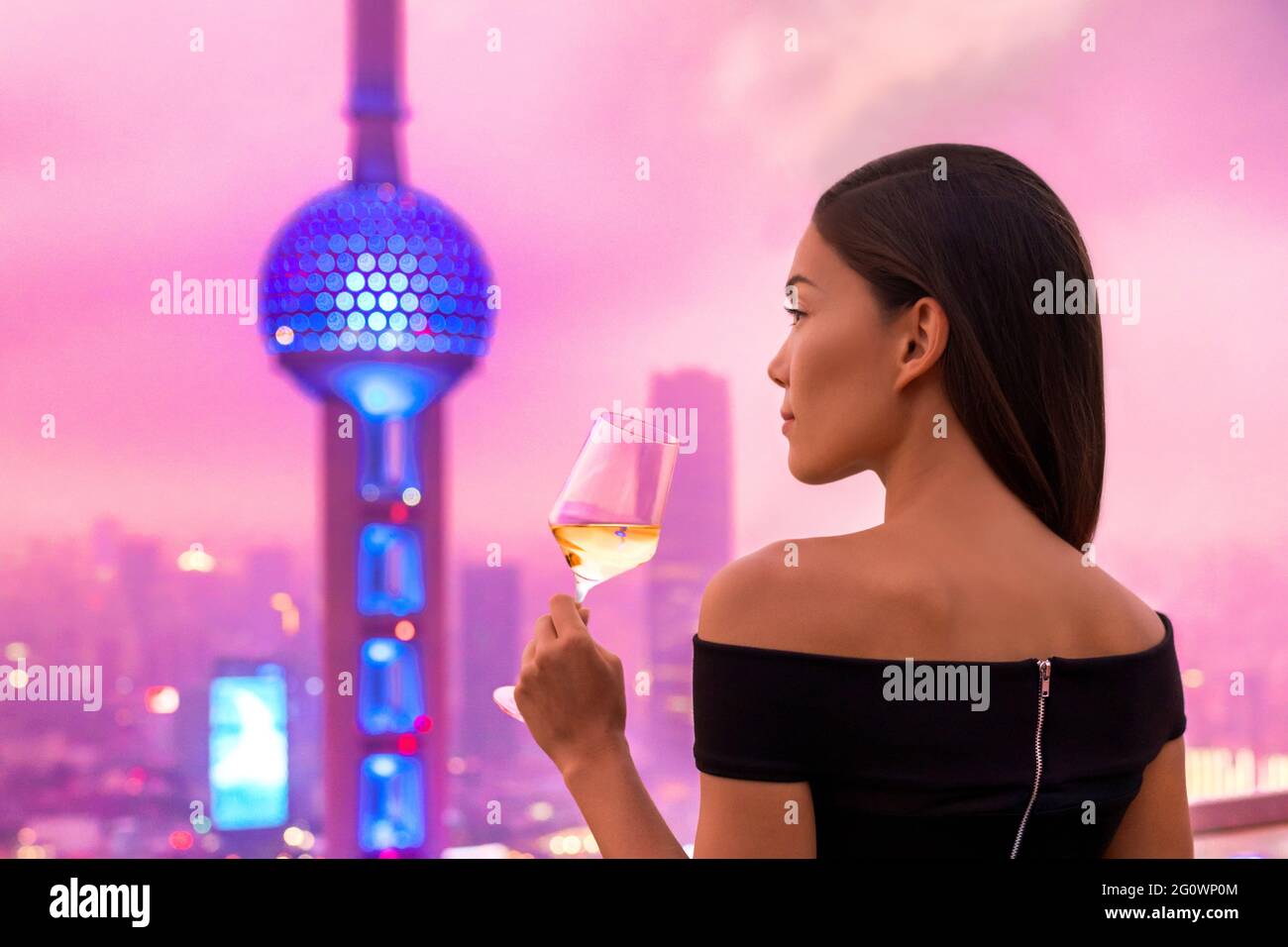 Elegante donna asiatica in abito da bere bicchiere di vino bianco sulla terrazza del bar sul tetto che guarda alla vista dell'orizzonte delle luci della città di Shanghai al tramonto. Viaggi di lusso Foto Stock