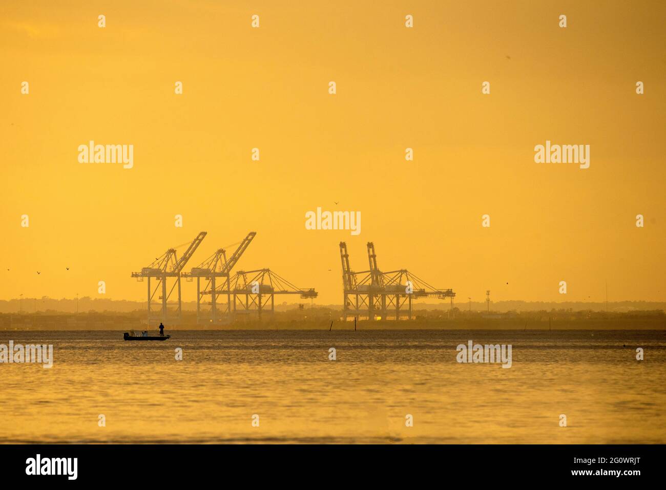 Un pescatore tenta la sua fortuna al tramonto sulla baia di Mobile in Alabama, Stati Uniti, con i cantieri navali in Mobile in aumento sullo sfondo. L'immagine è stata acquisita Foto Stock