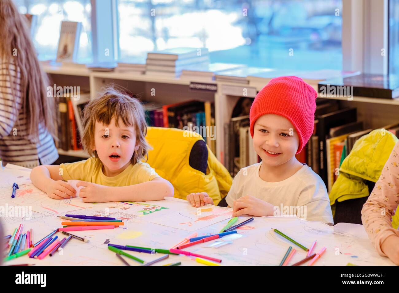 Felici i bambini che disegnano con i pastelli colorati mentre si siedono al tavolo nella stanza dell'asilo Foto Stock