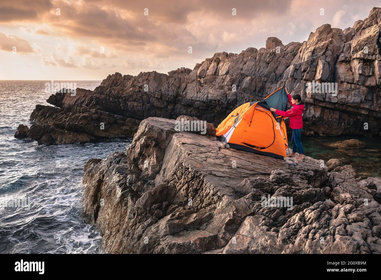 Femmina che istituisce tenda foe campeggio sulla roccia sopra il mare. Escursioni e campeggio all'aperto. Foto Stock
