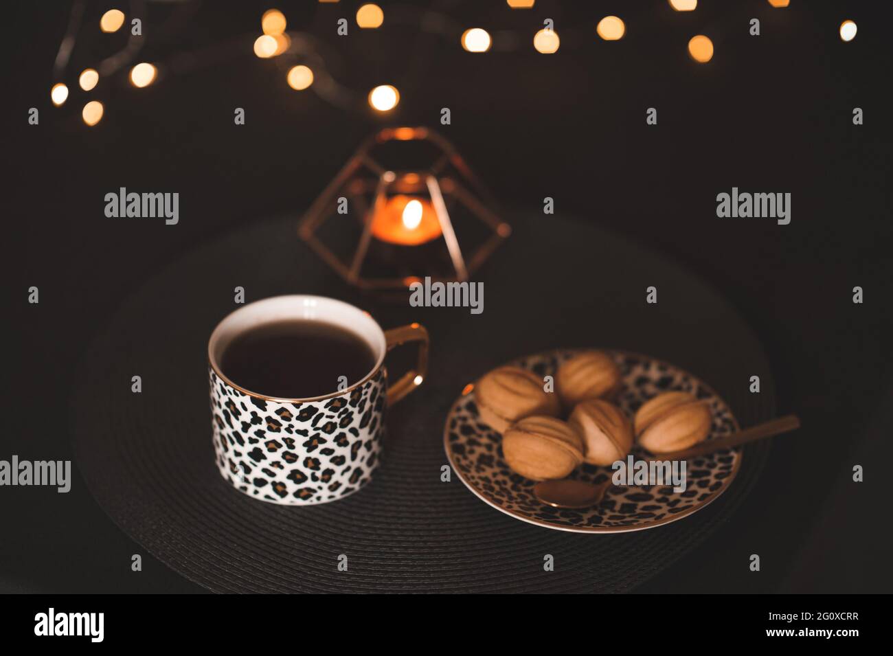 Tazza di tè fresco con gustosa pasticceria sul piatto con candela bruciante e closeup luci di Natale. Stagione invernale. Accogliente atmosfera familiare. Celebrazione Foto Stock