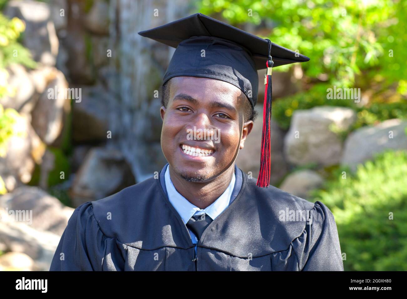 Bello giovane laureato nero che indossa cappuccio e abito sorridente orgogliosamente Foto Stock