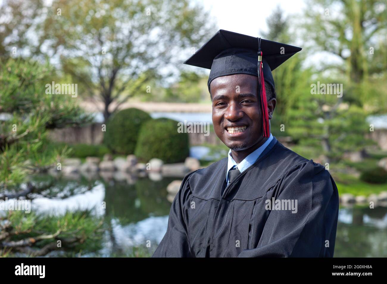 Bello giovane laureato nero che indossa cappuccio e abito sorridente orgogliosamente Foto Stock