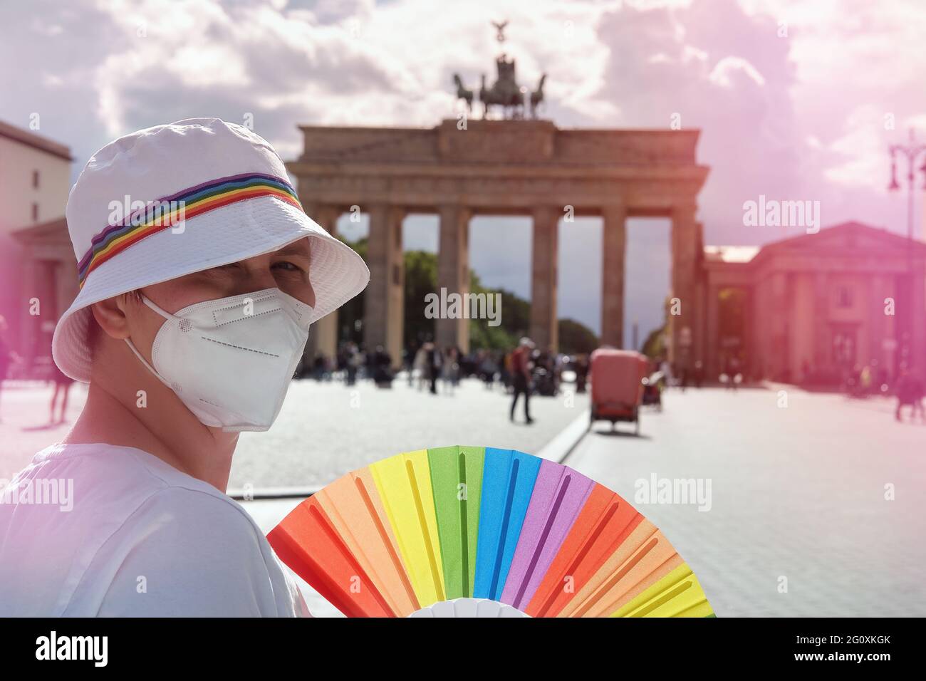Donna LGBT caucasica matura a Berlino con ventola arcobaleno e nastro su cappello estivo bianco. Rainbow, simbolo dell'orgoglio gay LGBTQIA, la diversità. Donna che indossa Foto Stock