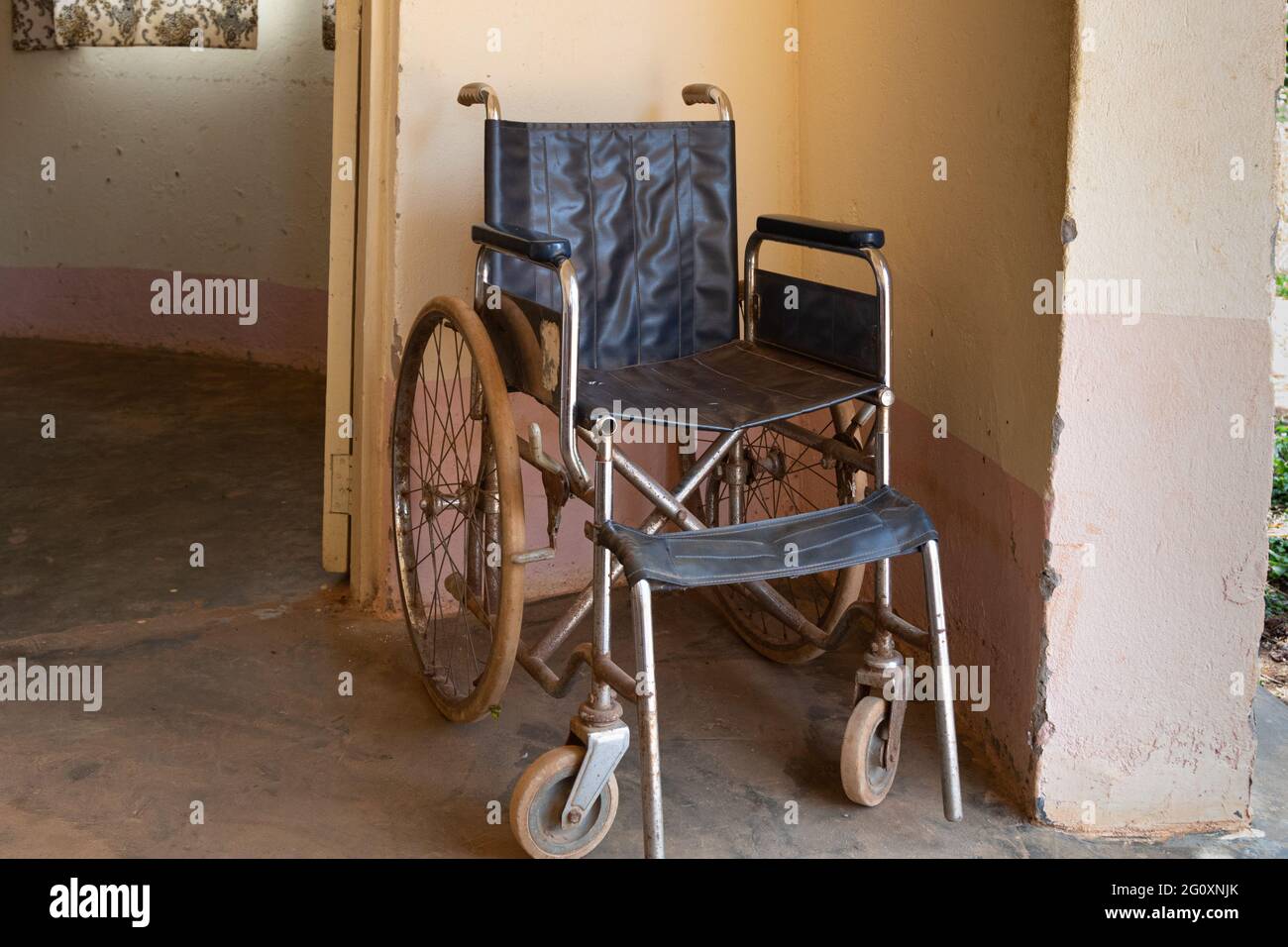 Una vecchia sedia a rotelle arrugginita si trova nel corridoio di un ospedale in Uganda Foto Stock