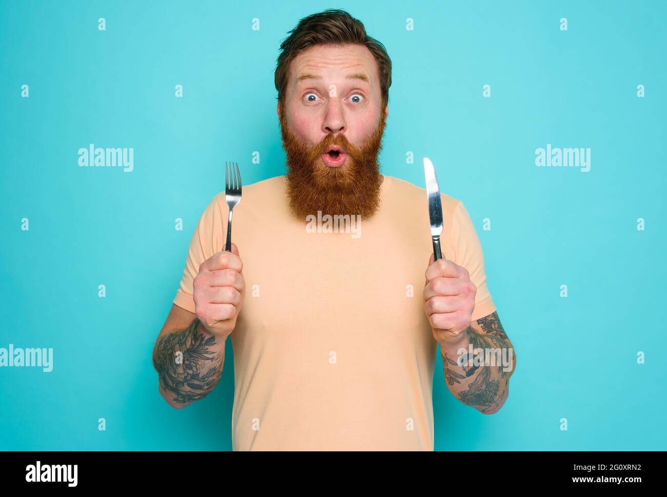 L'uomo con tatuaggi è pronto a mangiare qualcosa con le posate in mano Foto Stock