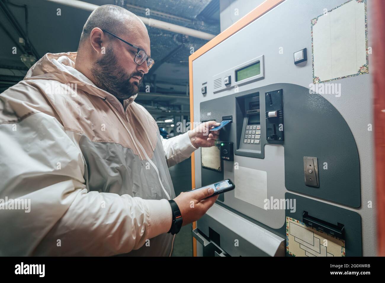 L'uomo paga per il parcheggio sotterraneo nel terminale di pagamento automatico del centro commerciale usando il suo telefono o la sua carta. Foto Stock