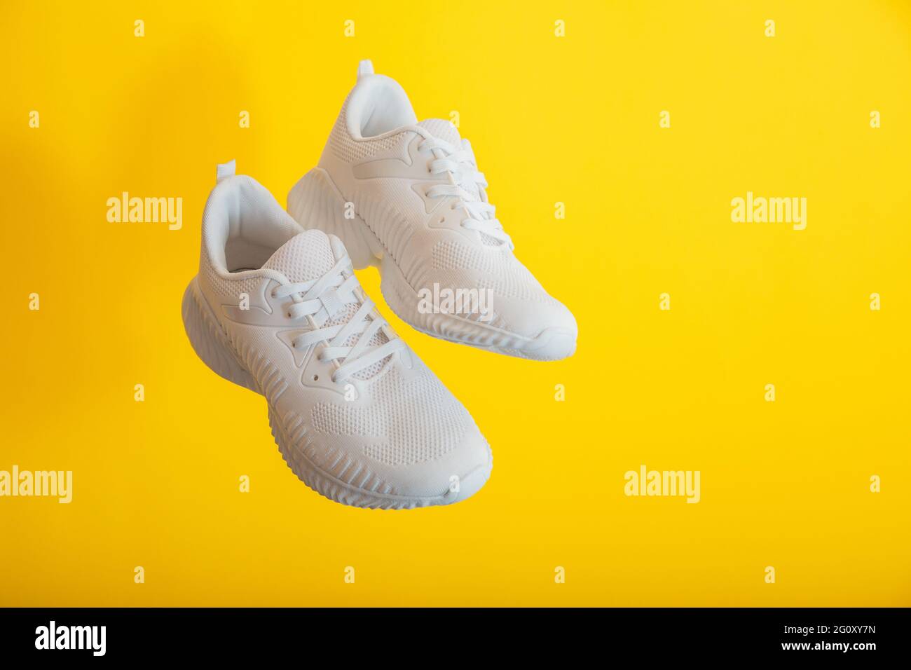 Scarpe sportive bianche levitazione su parete gialla. Le scarpe da ginnastica bianche volano su sfondo giallo con spazio per la copia. Paio di sneaker sportive maschili Foto Stock