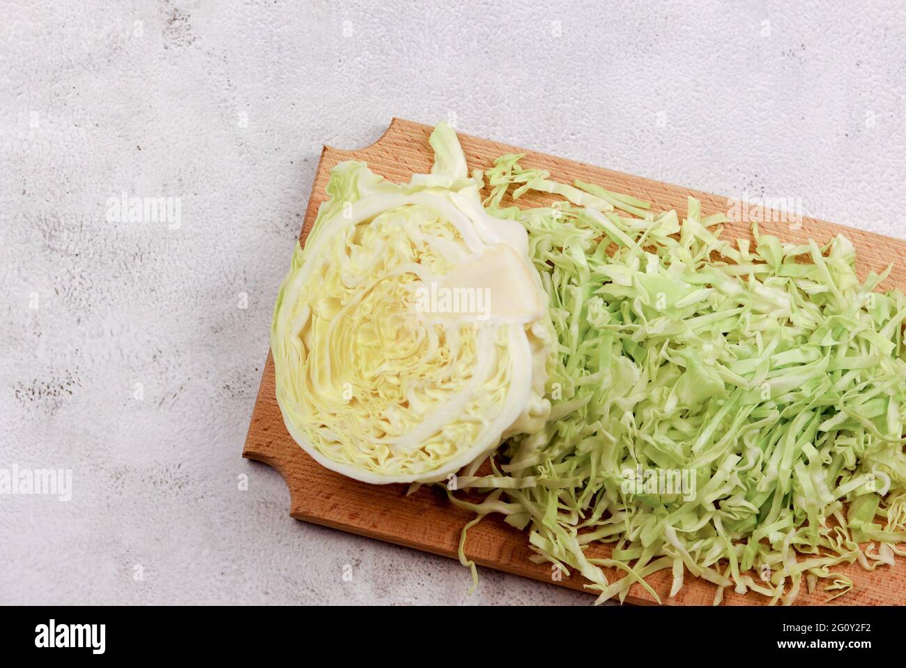 Metà della testa del giovane cavolo bianco triturato sul tagliere di legno su sfondo grigio chiaro. Vista dall'alto, disposizione piatta Foto Stock