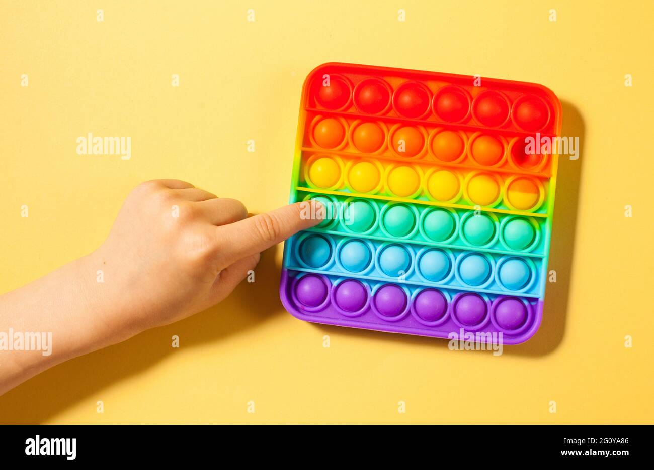 La mano di un bambino preme sul silicone giocattolo del pop su uno sfondo giallo. Giocattolo antistress, una tendenza nei giocattoli per bambini. Foto Stock